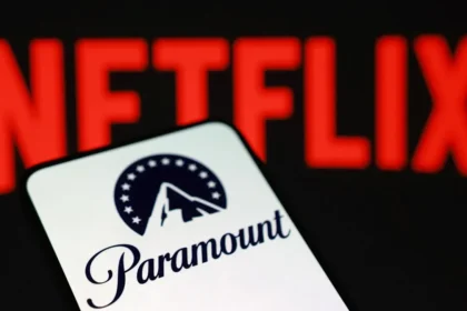 A close-up of a digital screen displaying the Netflix and Warner Bros. Discovery logos side-by-side with a legal gavel in the blurred background, illustrating the Netflix Warner Bros acquisition investigation.