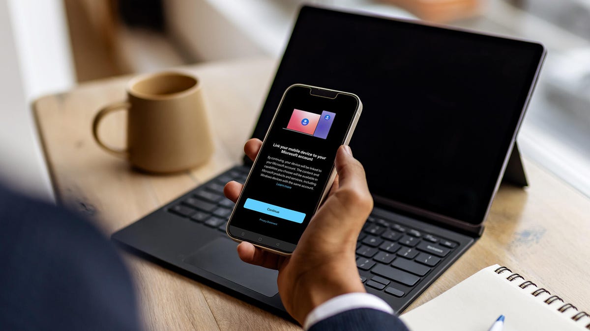 A person using a Windows 11 laptop while their Android smartphone interface is mirrored on the screen via Microsoft Phone Link