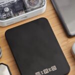 A sleek Anker Qi2 power bank magnetically attached to the back of a Google Pixel 10 Pro XL on a wooden desk.