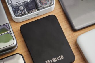 A sleek Anker Qi2 power bank magnetically attached to the back of a Google Pixel 10 Pro XL on a wooden desk.