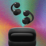 Detailed close-up of the Sony LinkBuds Clip open-ear headphones resting beside their compact, cookie-style charging case on a wooden desk.