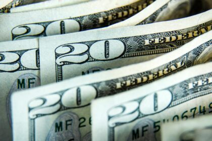 A person sitting at a modern wooden desk holding a credit card while comparing various AI chatbot interfaces on a dual-monitor setup in a bright home office.