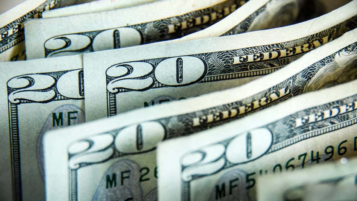 A person sitting at a modern wooden desk holding a credit card while comparing various AI chatbot interfaces on a dual-monitor setup in a bright home office.