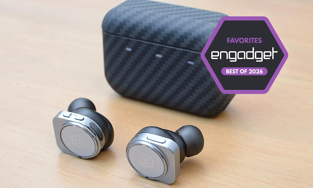 A close-up of a traveler wearing sleek black noise-canceling earbuds while sitting in a crowded, blurred-out international airport terminal.