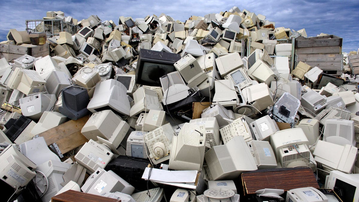 A person handing over a stack of old laptops and tangled chargers to a retail store employee for recycling