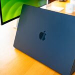 A sleek silver MacBook Pro displaying the Reins app interface alongside a terminal window running Ollama local models in a bright office.