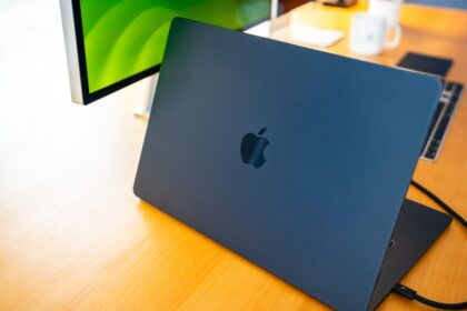 A sleek silver MacBook Pro displaying the Reins app interface alongside a terminal window running Ollama local models in a bright office.