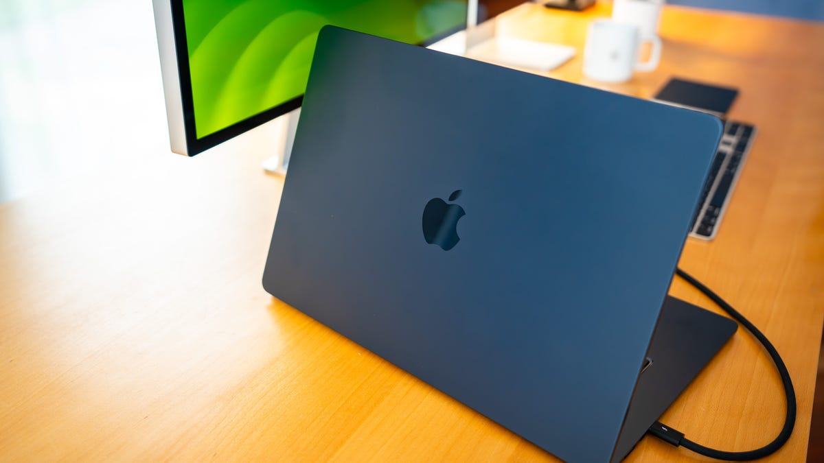 A sleek silver MacBook Pro displaying the Reins app interface alongside a terminal window running Ollama local models in a bright office.