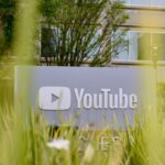 A person sitting in a dimly lit living room using a voice-activated remote to interact with the YouTube Gemini AI interface on a 4K smart TV.