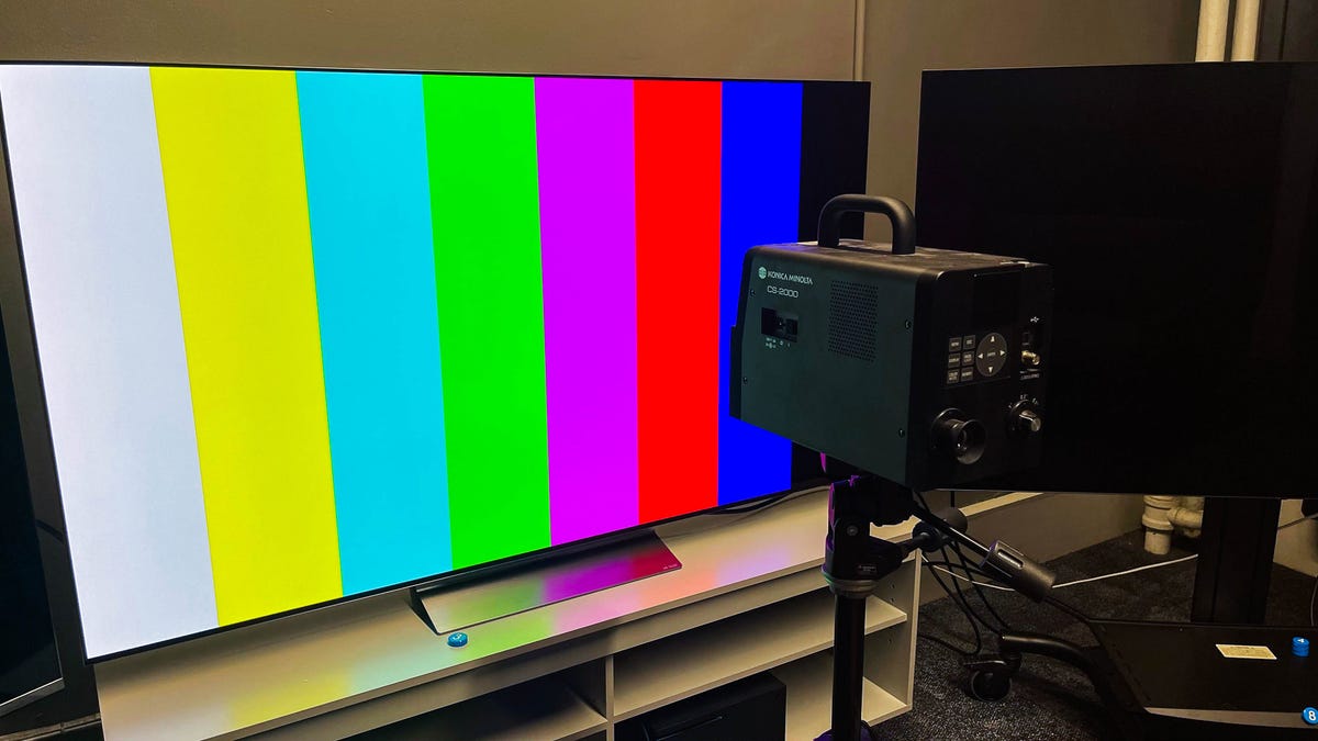 Reviewer calibrating a modern OLED television panel in a dark testing laboratory using specialized spectroradiometer equipment.