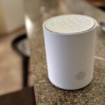 A sleek white SimpliSafe entry sensor and a modern smart camera mounted on a contemporary wooden door frame during a 2026 home security installation.