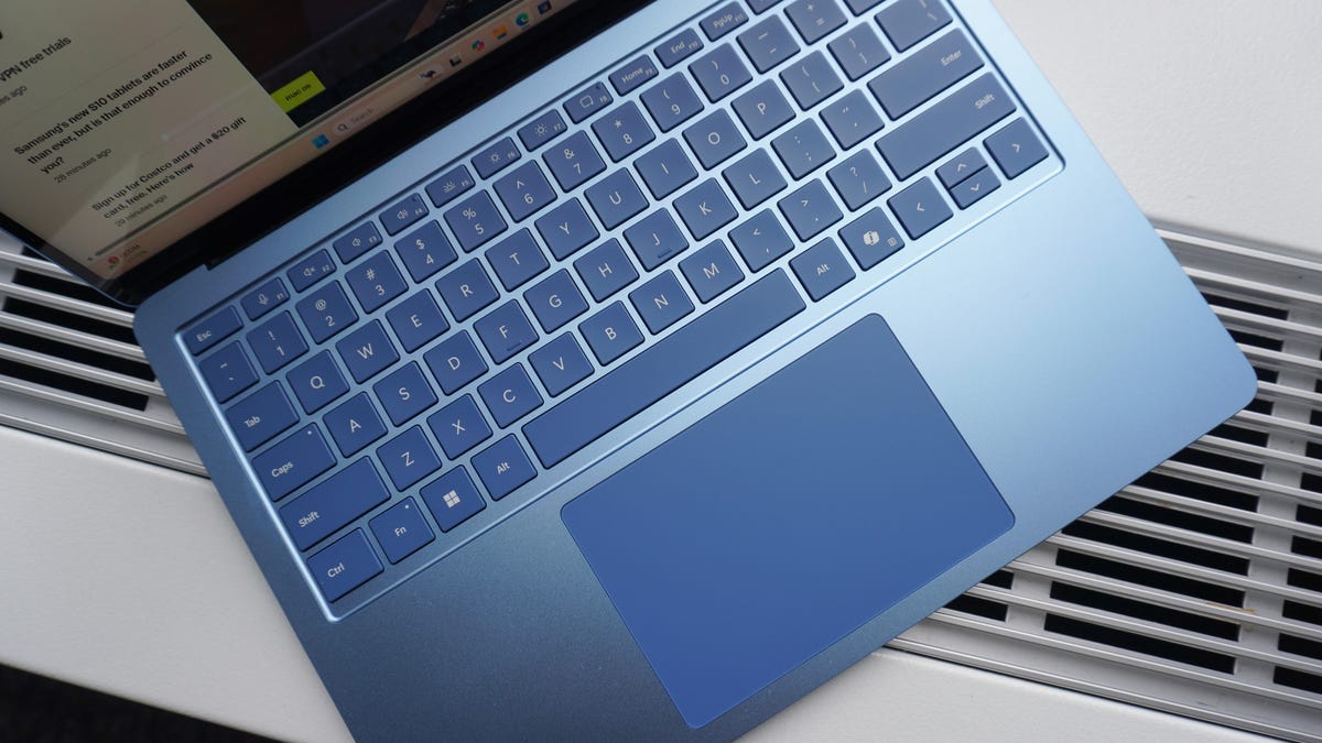 A close-up of a person's hands hovering over a backlit mechanical keyboard with a Windows 11 interface blurred in the background.