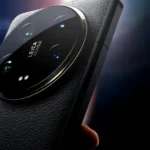 Close-up of a sleek ceramic smartphone camera module with Leica branding resting on a wooden table in a sunlit cafe